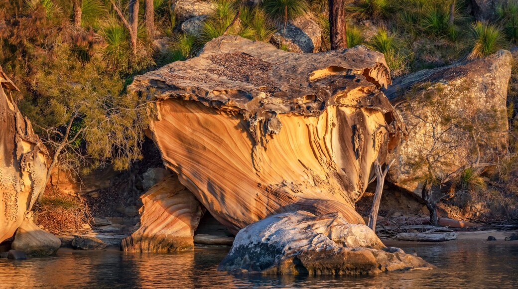A large rock formation with a river flowing around it, surrounded by greenery and trees.