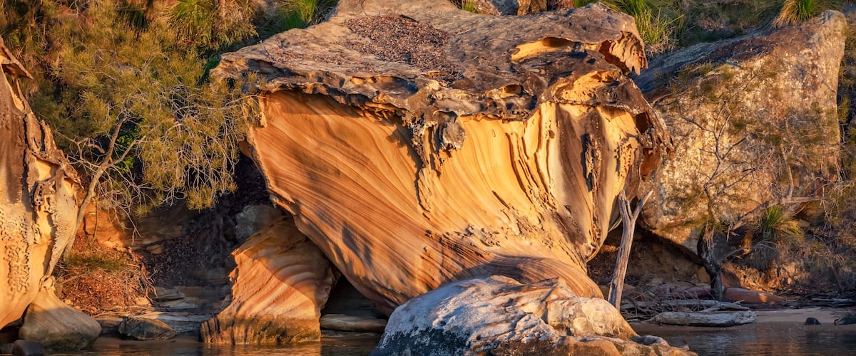 A large rock formation with a river flowing around it, surrounded by greenery and trees.
