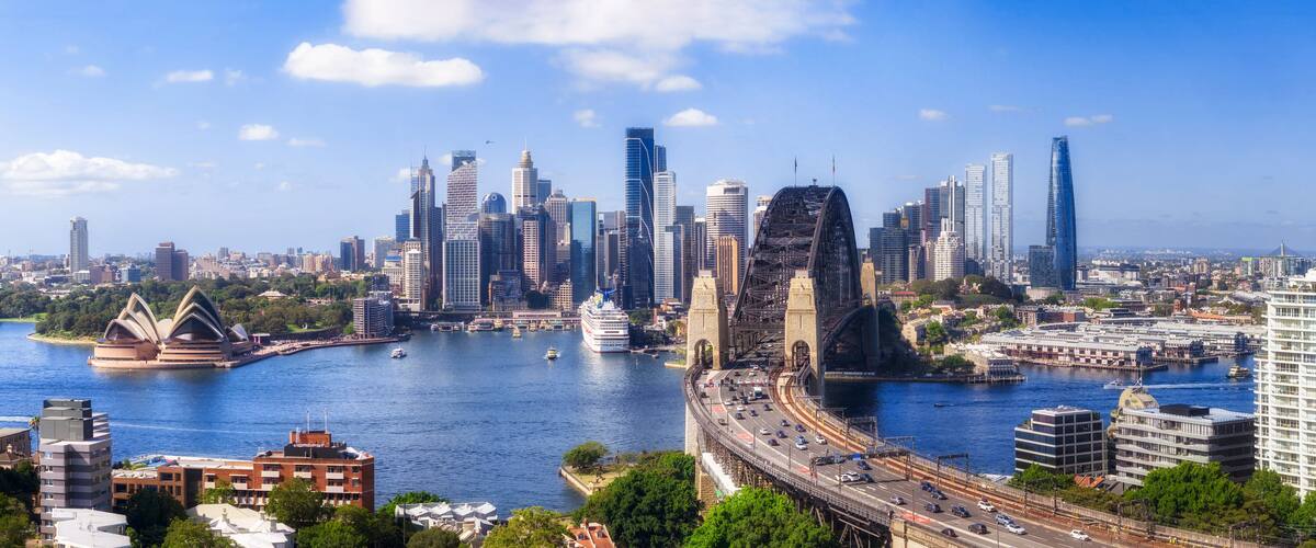 Stadsbeeld met moderne wolkenkrabbers, een brug en het Sydney Opera Huis aan het water.