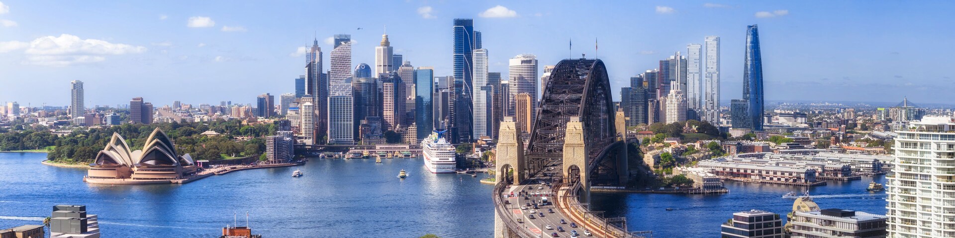 Silhueta urbana com arranha-céus modernos, uma ponte e a Ópera de Sydney à beira da água.