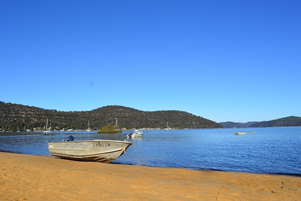 A boat on a sandy beach, a calm lake, and hills in the background.