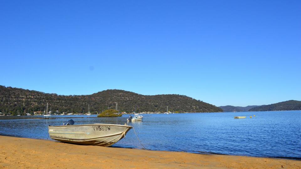 A boat on a sandy beach, a calm lake, and hills in the background.