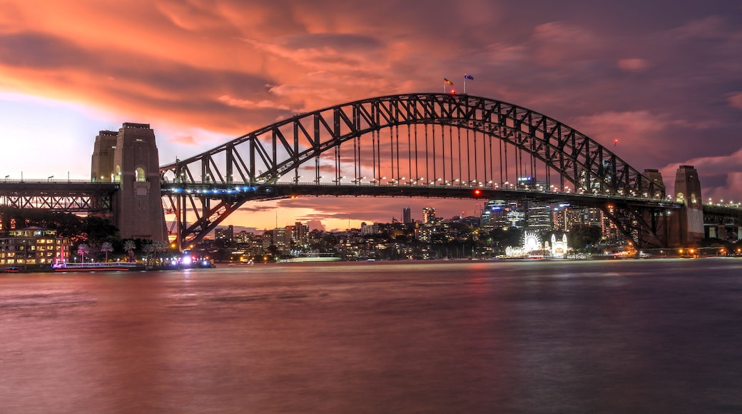 A large suspension bridge with two towers, spanning over a body of water with a cityscape in the background.