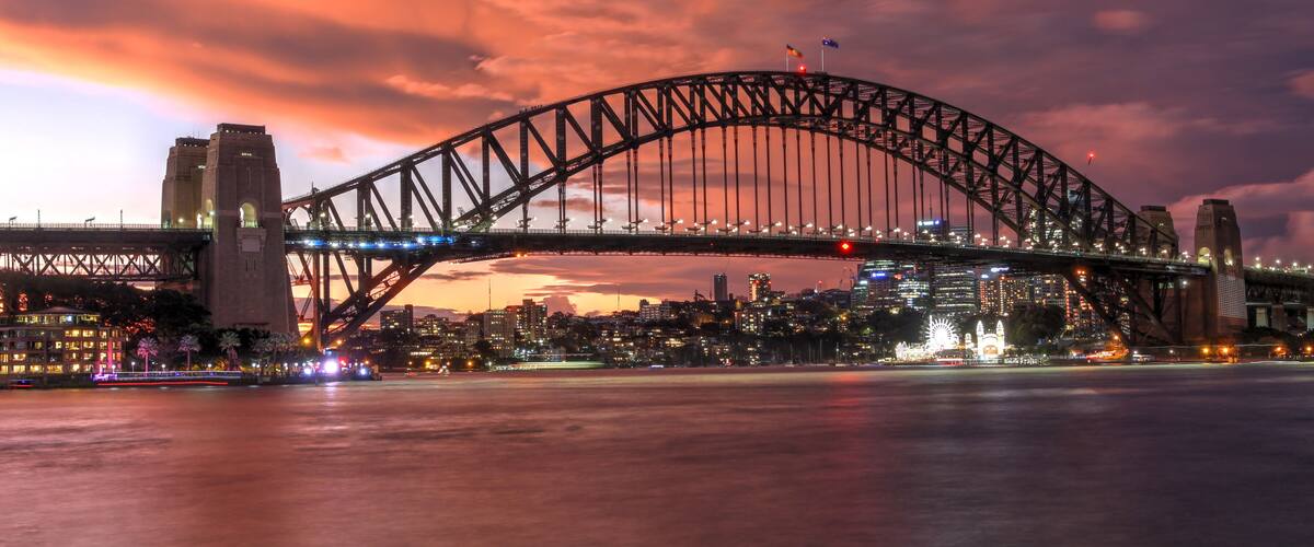 A large suspension bridge with two towers, spanning over a body of water with a cityscape in the background.