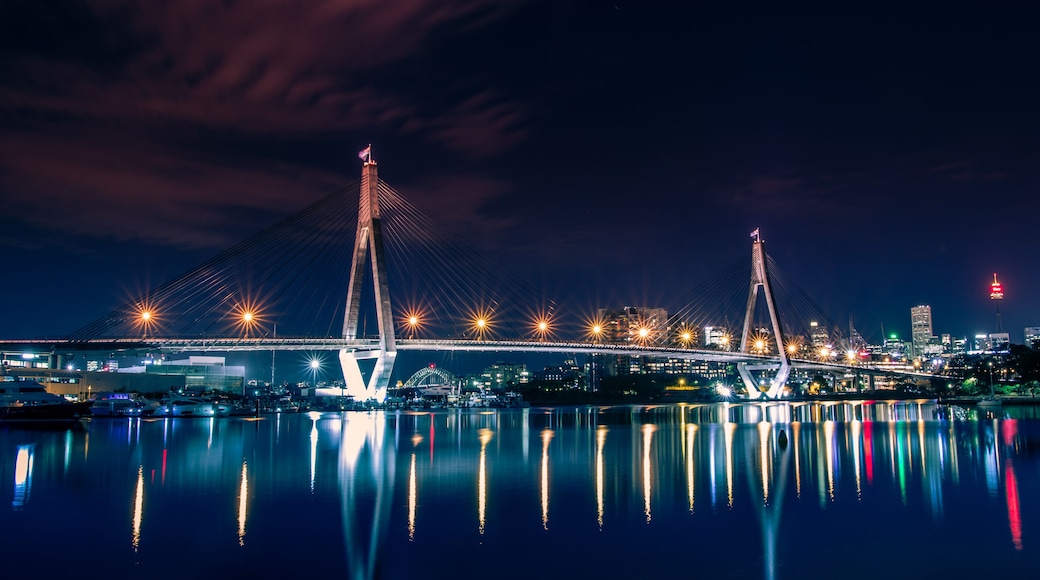 Vue nocturne d’un pont à haubans dont les lumières se reflètent sur l’eau.