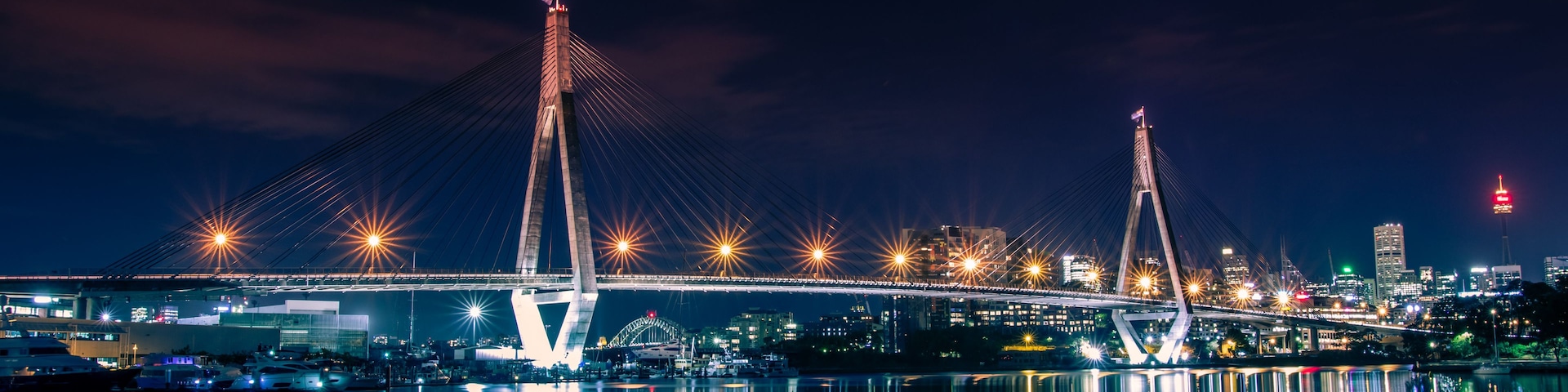 Vista noturna de uma ponte atirantada, com suas luzes refletindo na água.