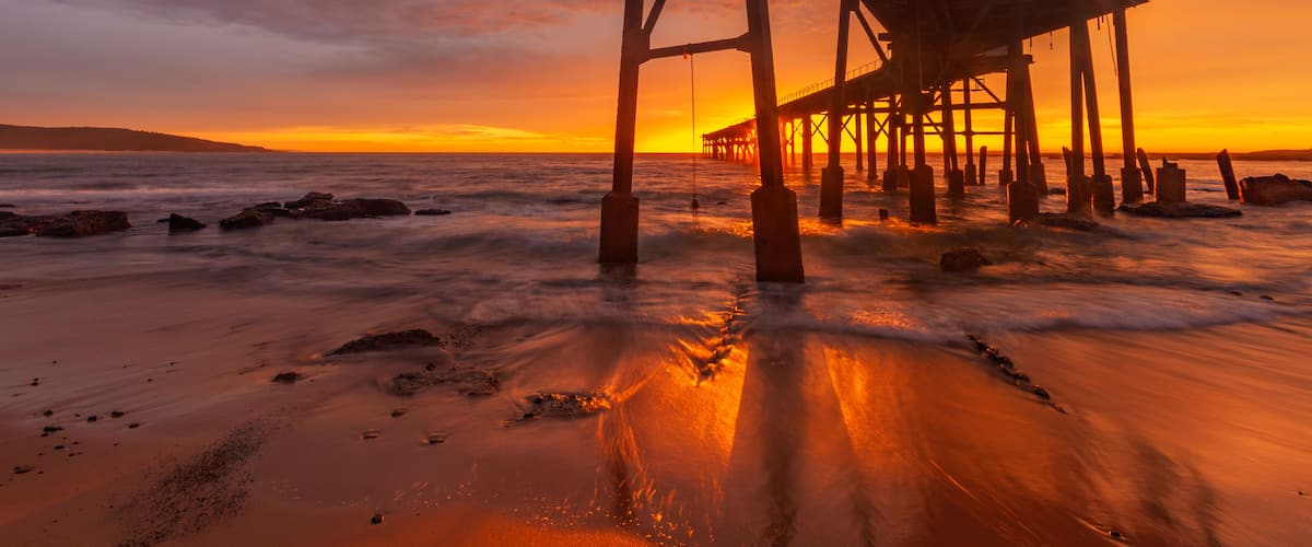 A pier extending into the ocean at sunset with waves crashing against it.