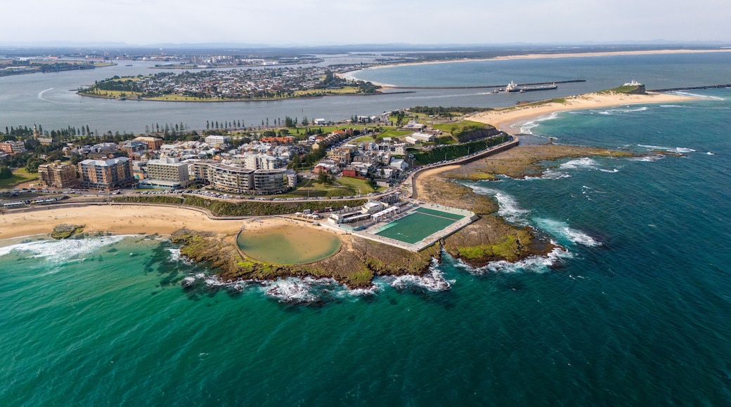 An aerial view of a coastal town with a beach, rocky shoreline, and a large building complex.