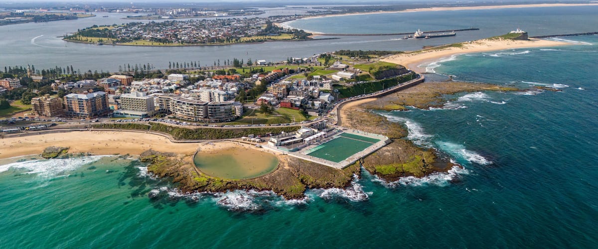 An aerial view of a coastal town with a beach, rocky shoreline, and a large building complex.