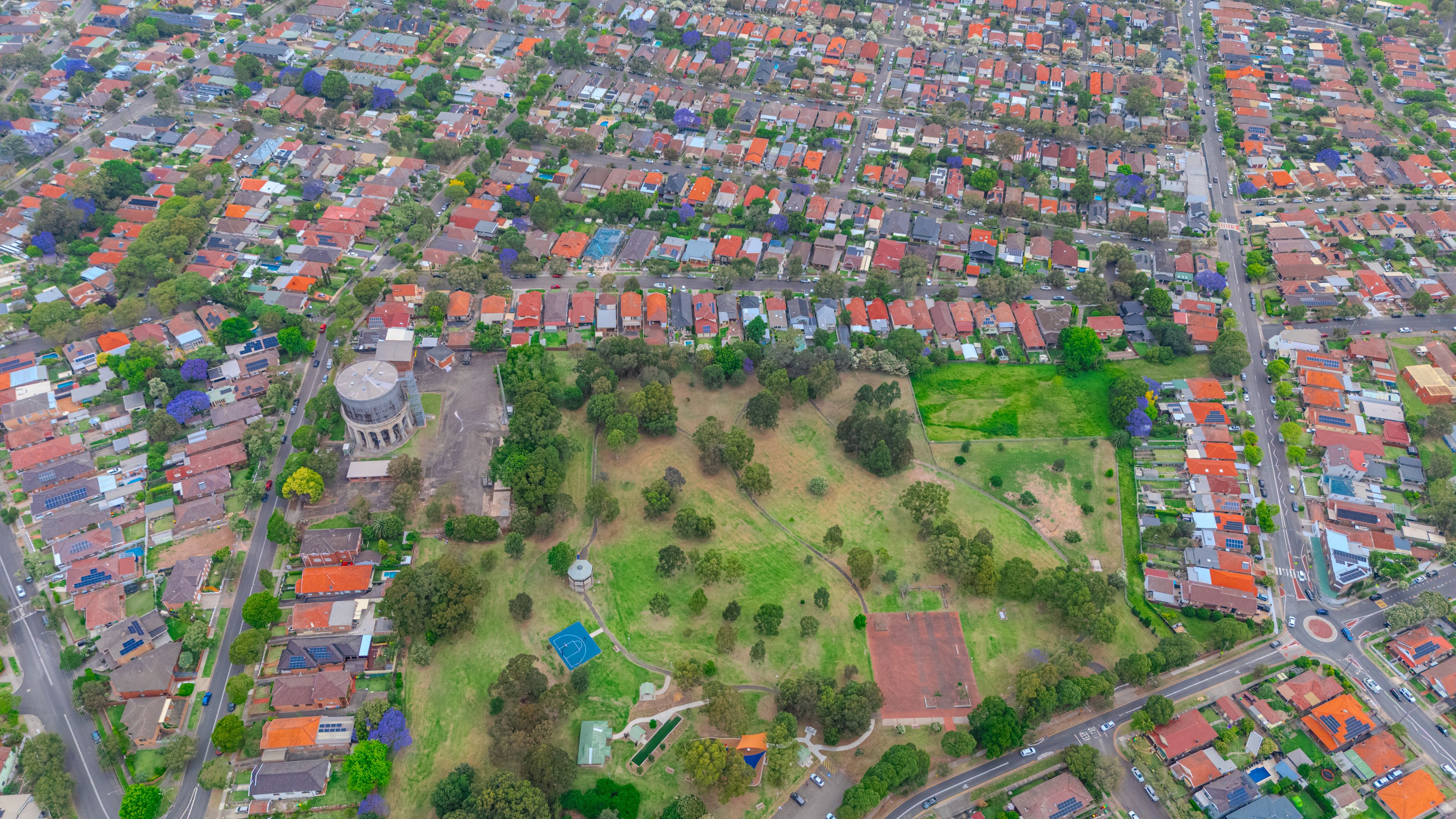 An aerial view of a residential area with houses, a large open field, and a circular building.