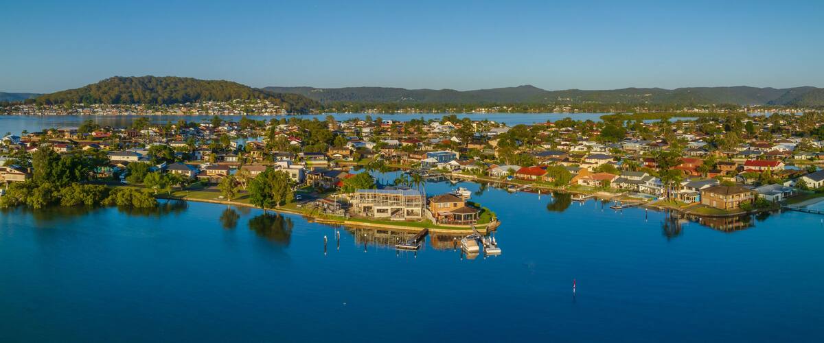 A coastal town with houses, a marina, and a hill in the background.