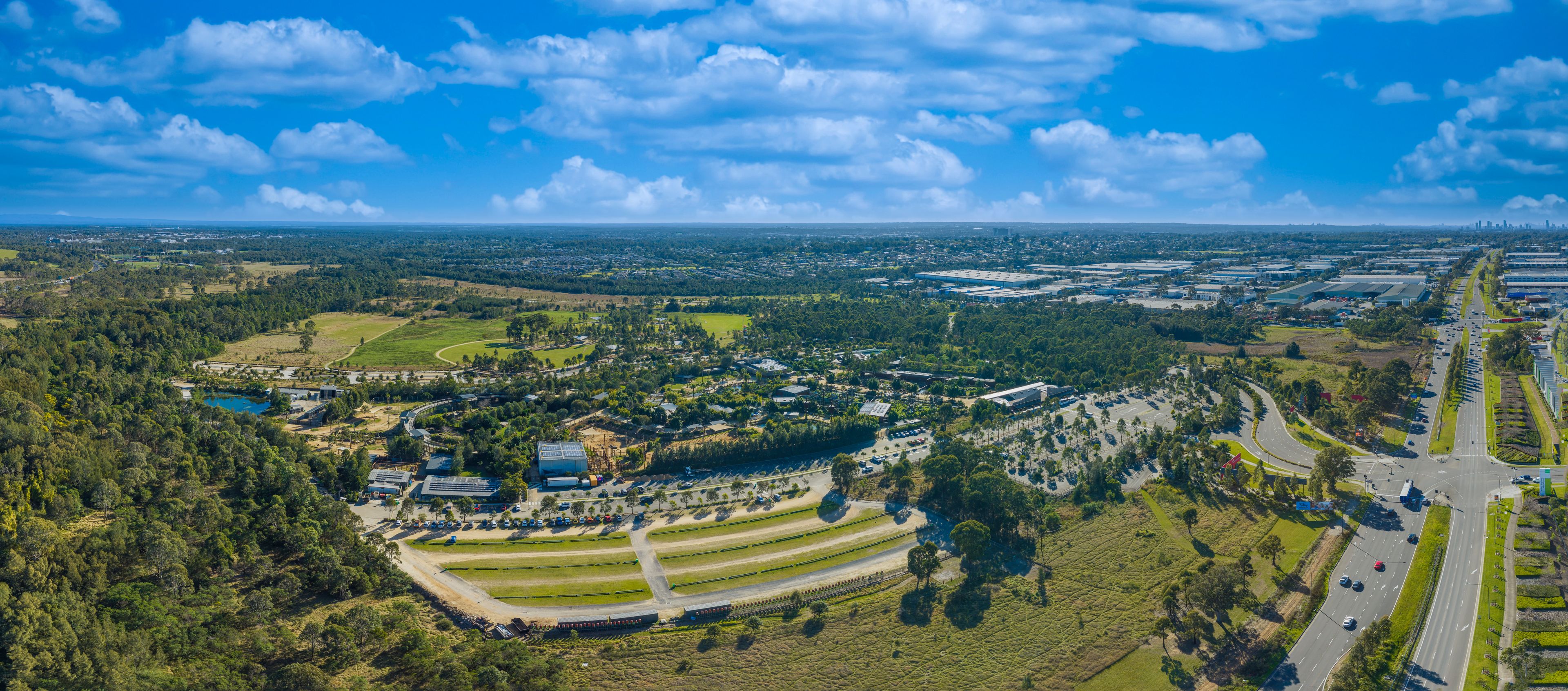 Vista aérea de uma área suburbana com edifícios residenciais, áreas verdes e uma autoestrada.