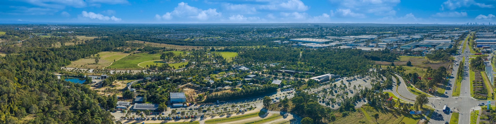 Vista aérea de uma área suburbana com edifícios residenciais, áreas verdes e uma autoestrada.