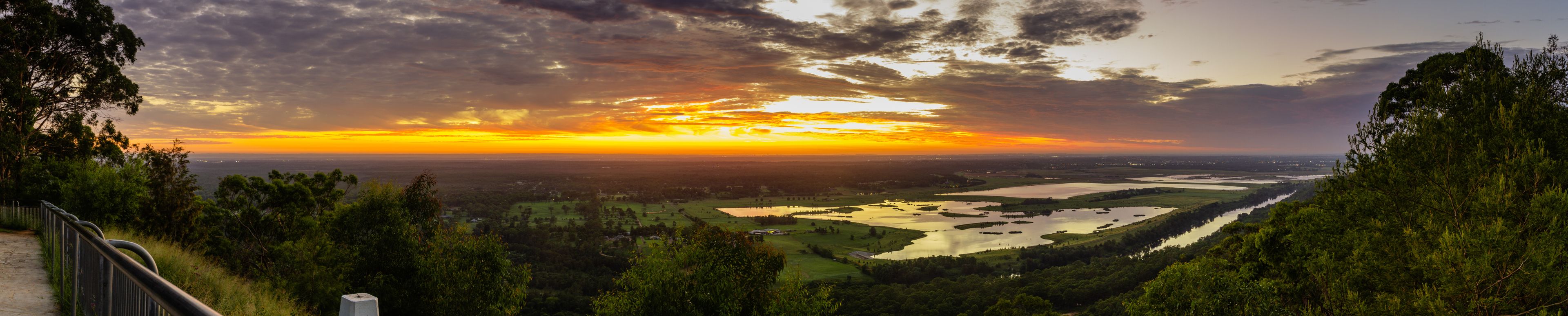 Un paisaje panorámico con un atardecer, un río y una zona boscosa.