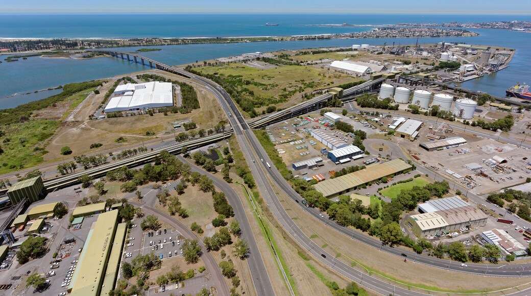 An aerial view of a coastal industrial area with a bridge, storage tanks, and a highway.