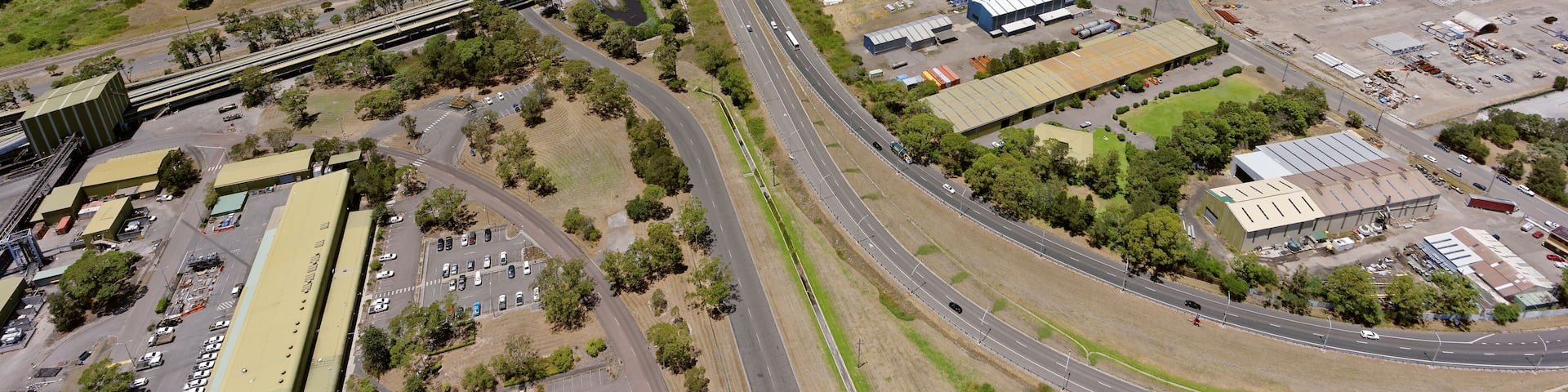 An aerial view of a coastal industrial area with a bridge, storage tanks, and a highway.