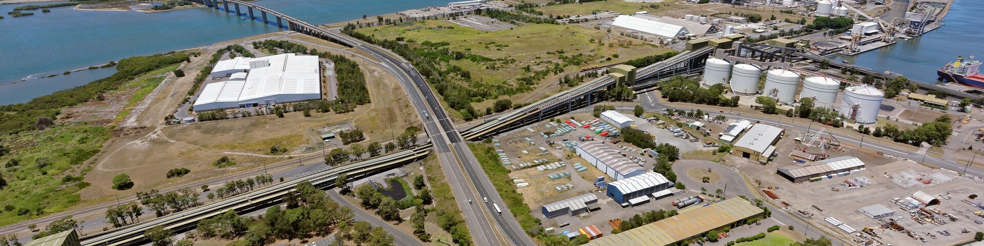 Eine Luftaufnahme eines Küstenindustrieteils mit einer Brücke, Lagertanks und einer Autobahn.