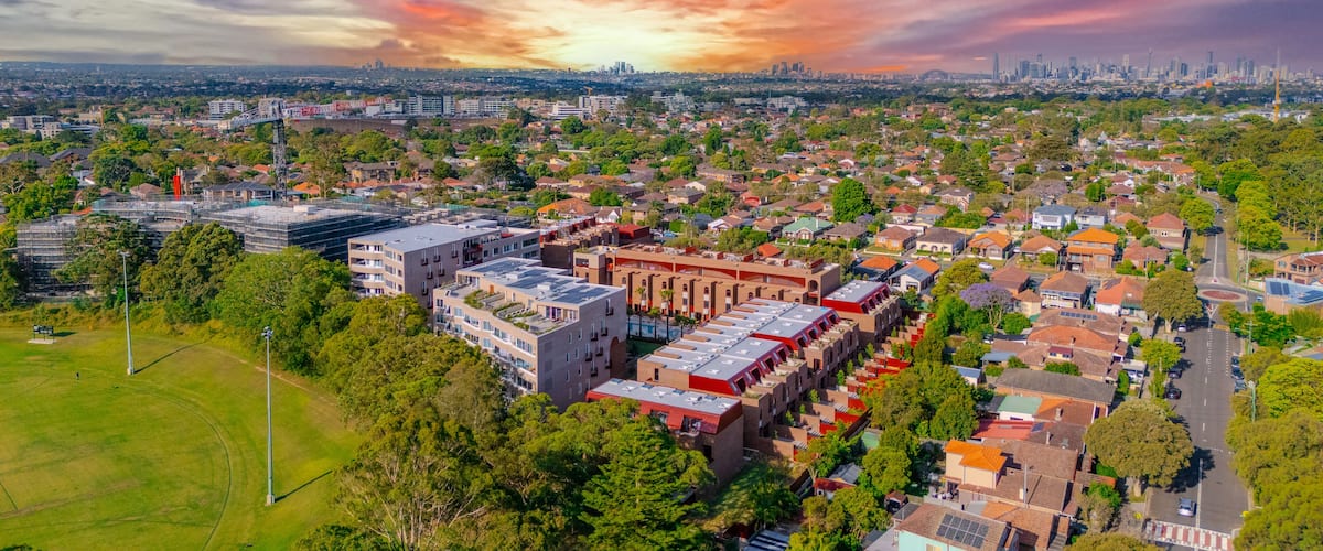 A cityscape with a sunset, featuring a mix of residential and commercial buildings, a prominent tower, and a green park area.