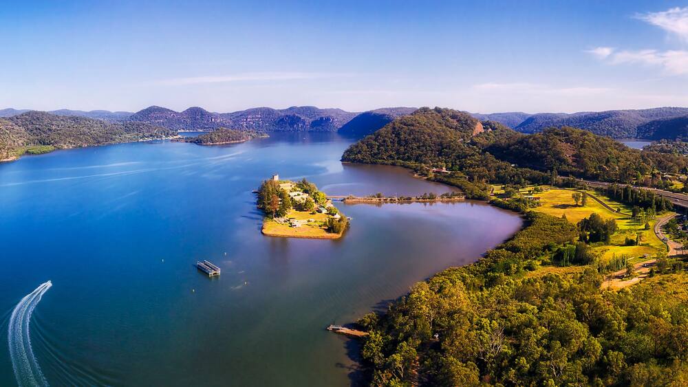 A large lake surrounded by hills, a small island, and a road with vehicles.