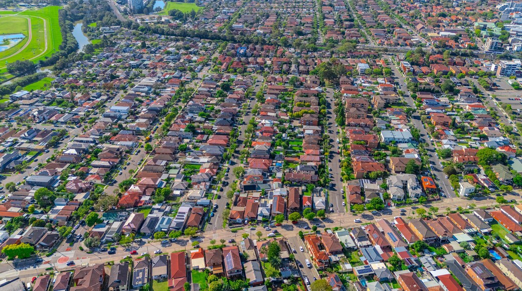 An aerial view of a densely populated residential area with uniform housing, green spaces, and a river.