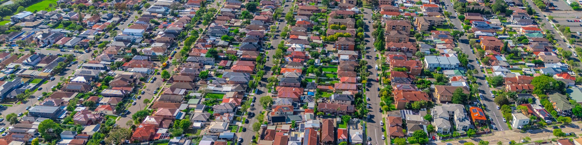 Vista aérea de uma área residencial densamente povoada, com casas padronizadas, áreas verdes e um rio.