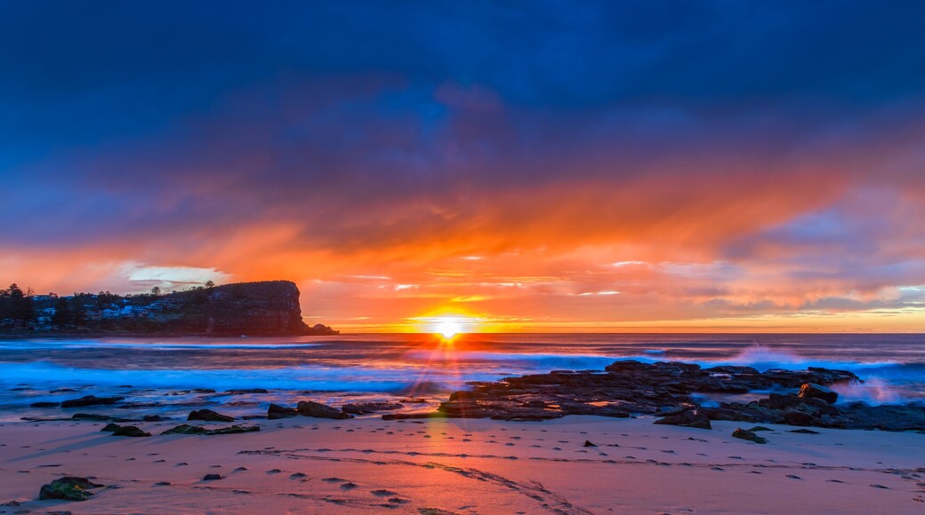 A sunset over a beach with rocks and a cliff.