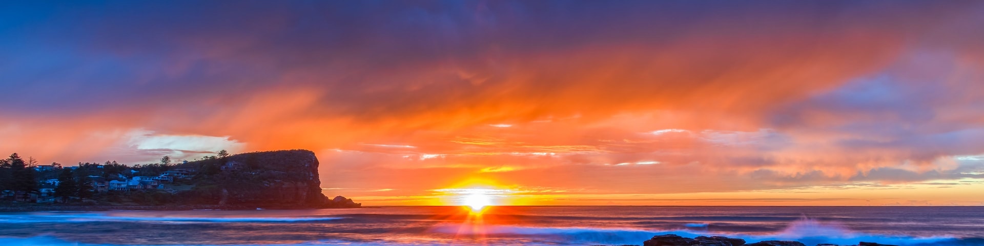 Un coucher de soleil sur une plage avec des rochers et une falaise.