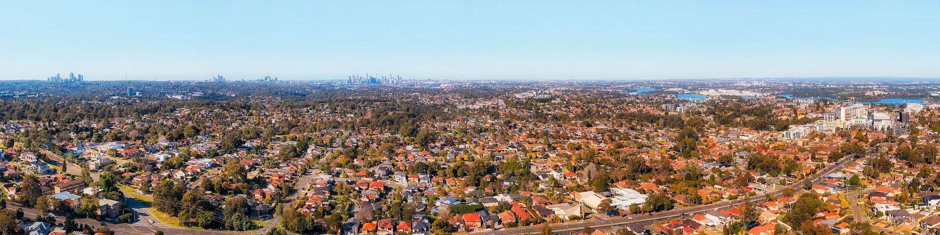 Une vue panoramique d’une ville, avec ses quartiers résidentiels densément peuplés, une autoroute importante et le profil de la ville en arrière-plan.