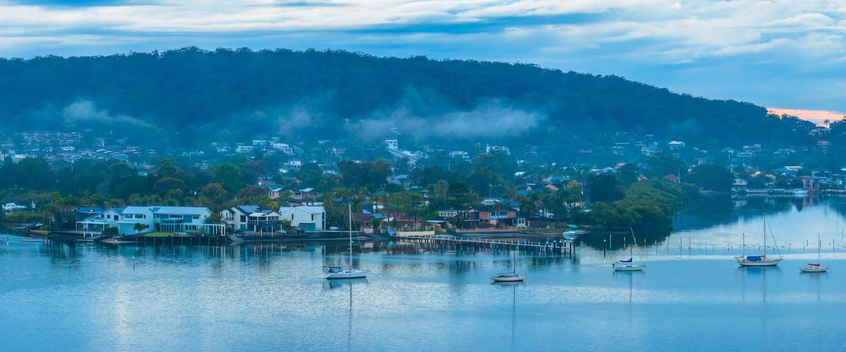 A coastal town with a marina, boats, and a forested hill in the background.