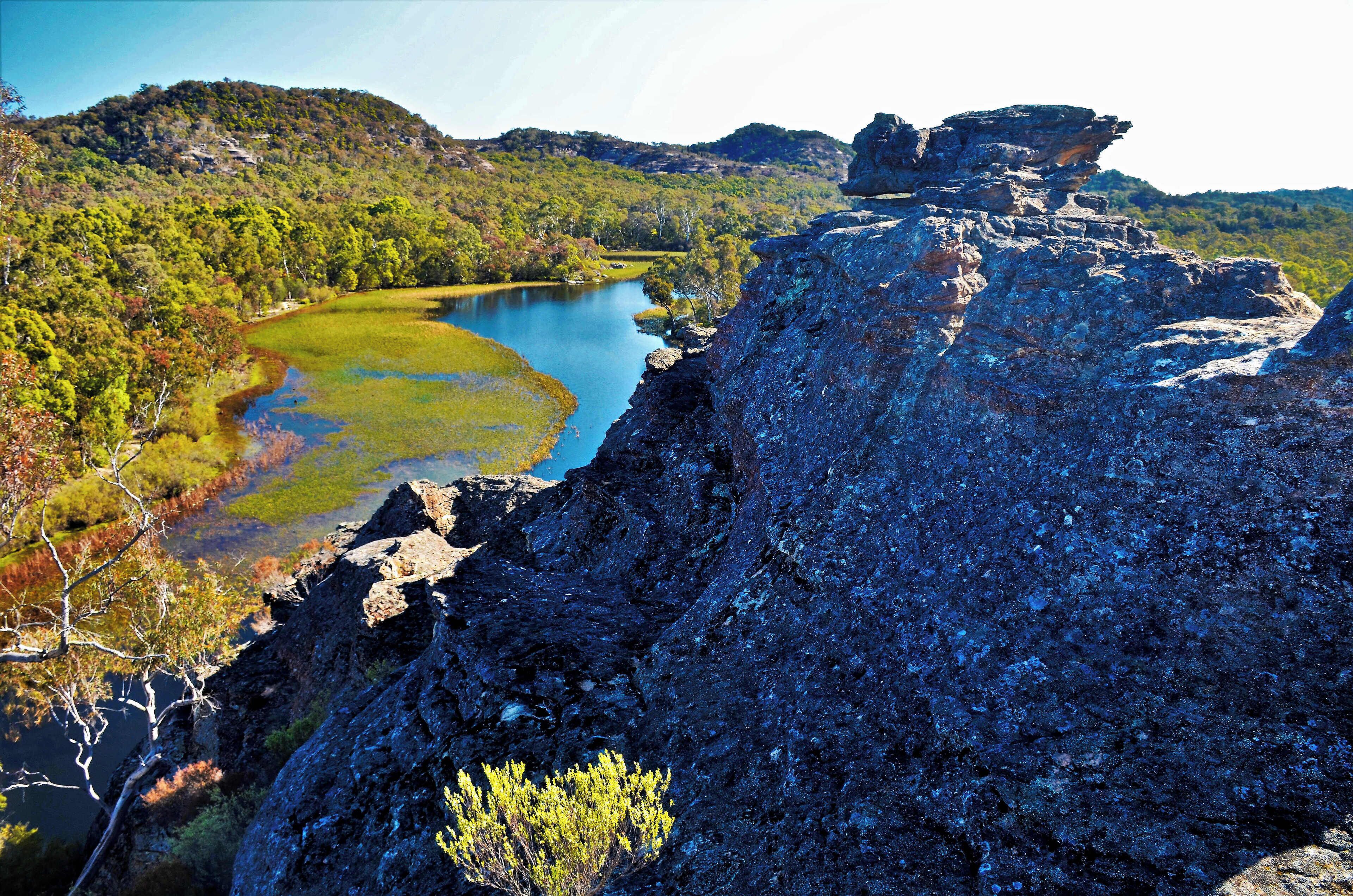 A rugged cliff overlooking a calm lake surrounded by dense forest and hills.