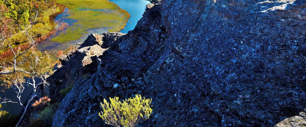 A rugged cliff overlooking a calm lake surrounded by dense forest and hills.