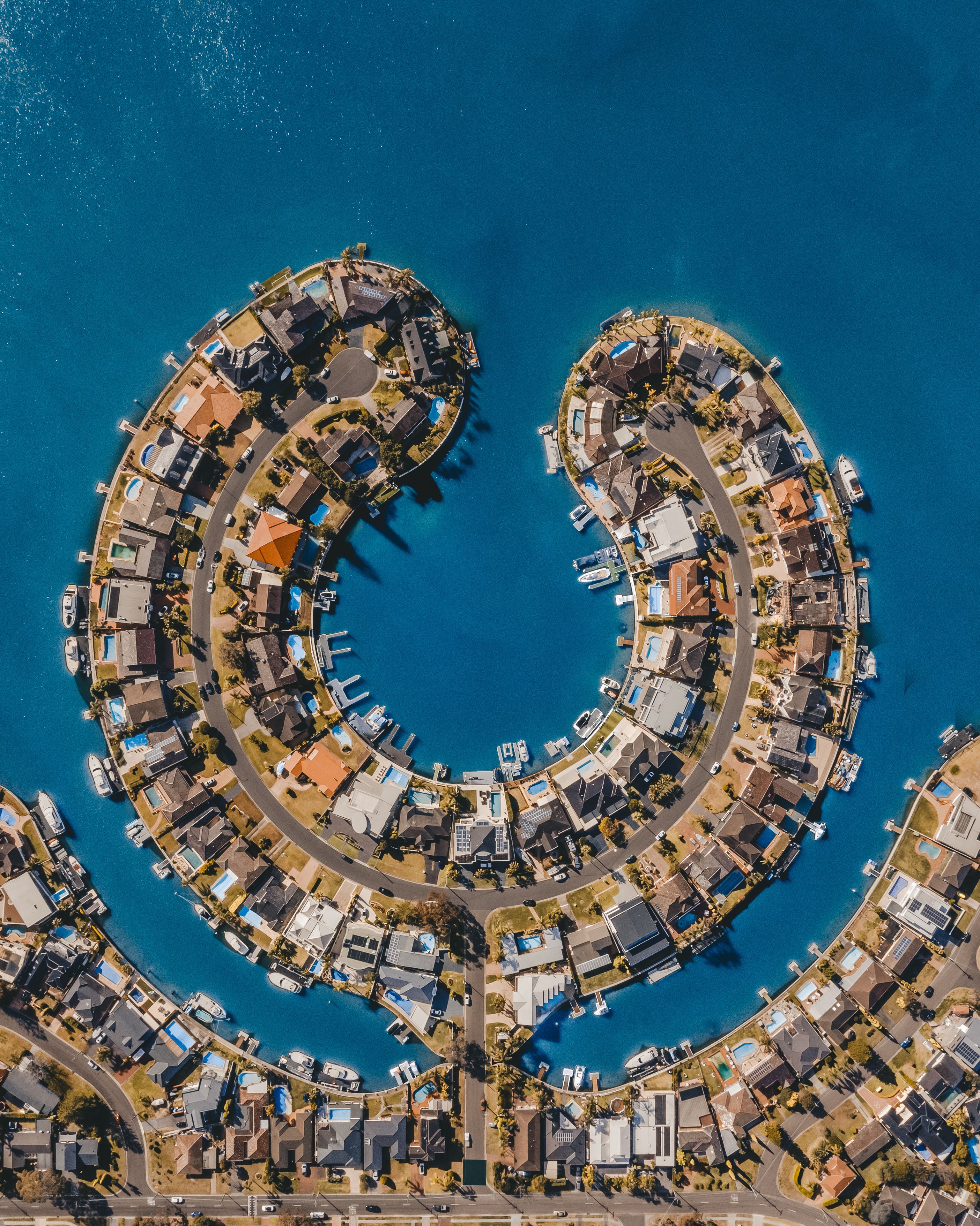 A coastal residential area with a circular layout of houses and boats docked along the waterfront.