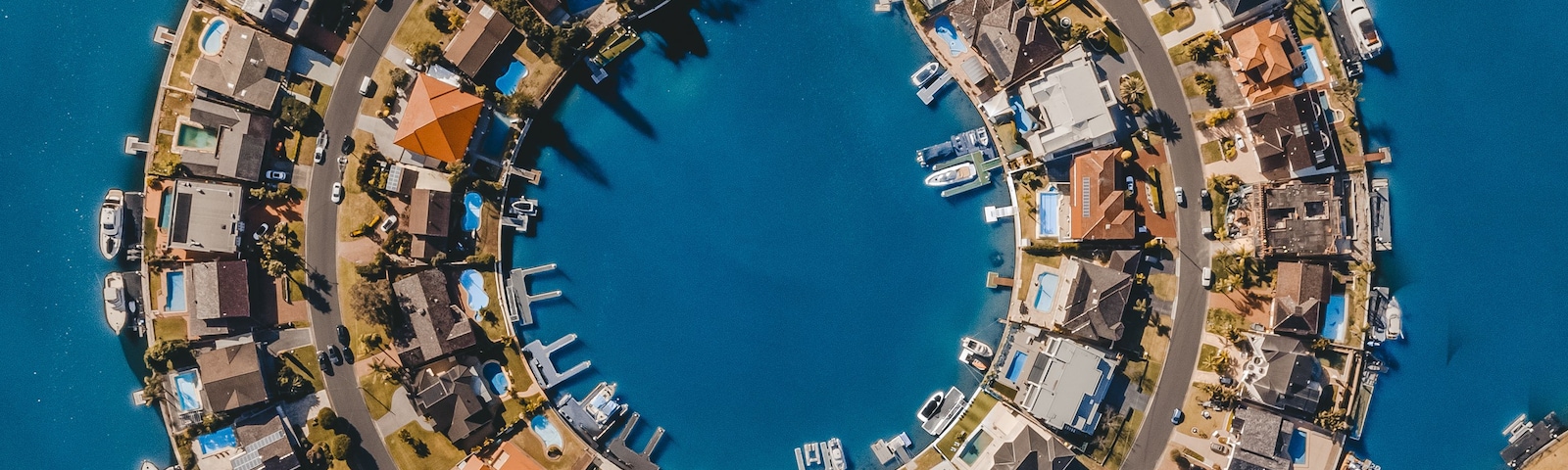 A coastal residential area with a circular layout of houses and boats docked along the waterfront.