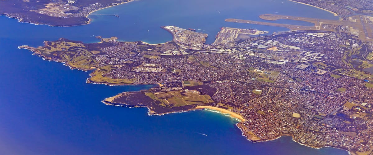 An aerial view of a coastal city with a dense urban area, a large body of water, and several islands.