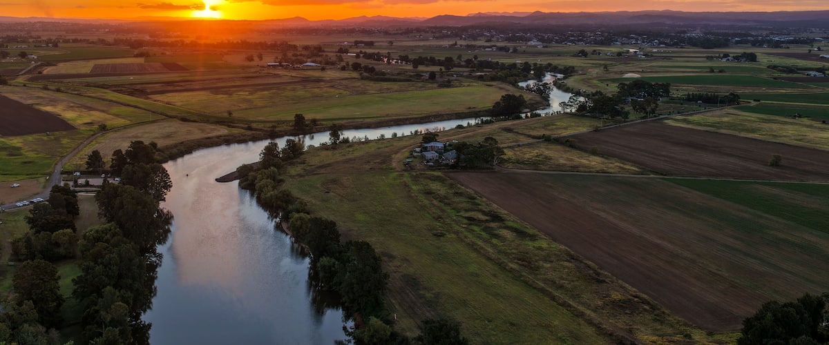 Un río serpentea a través de un paisaje rural con campos y una puesta de sol al fondo.