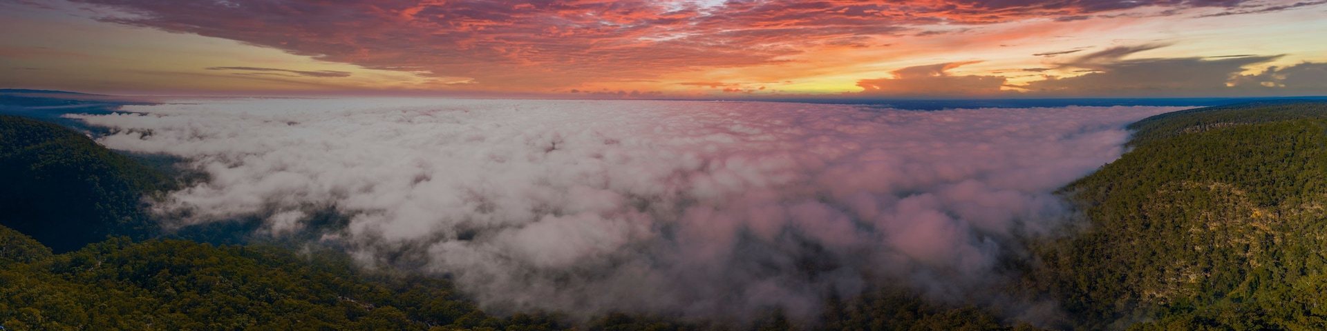 Paisagem montanhosa com um vale coberto de nuvens e céu ao pôr do sol.