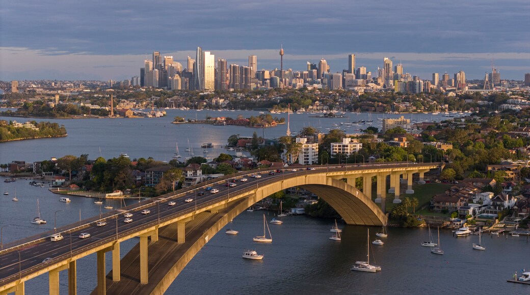 A bridge over a river with boats, a city skyline in the background, and a clear sky.