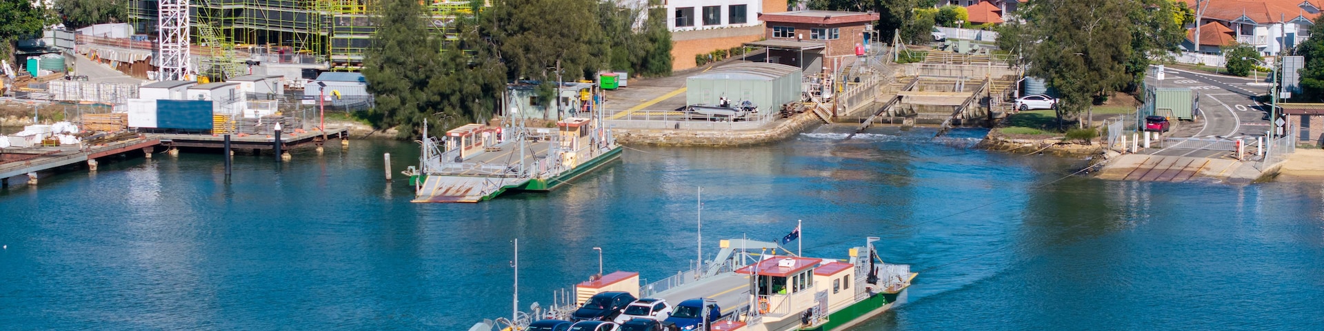 A green and white ferry docked at a pier with a cityscape in the background.