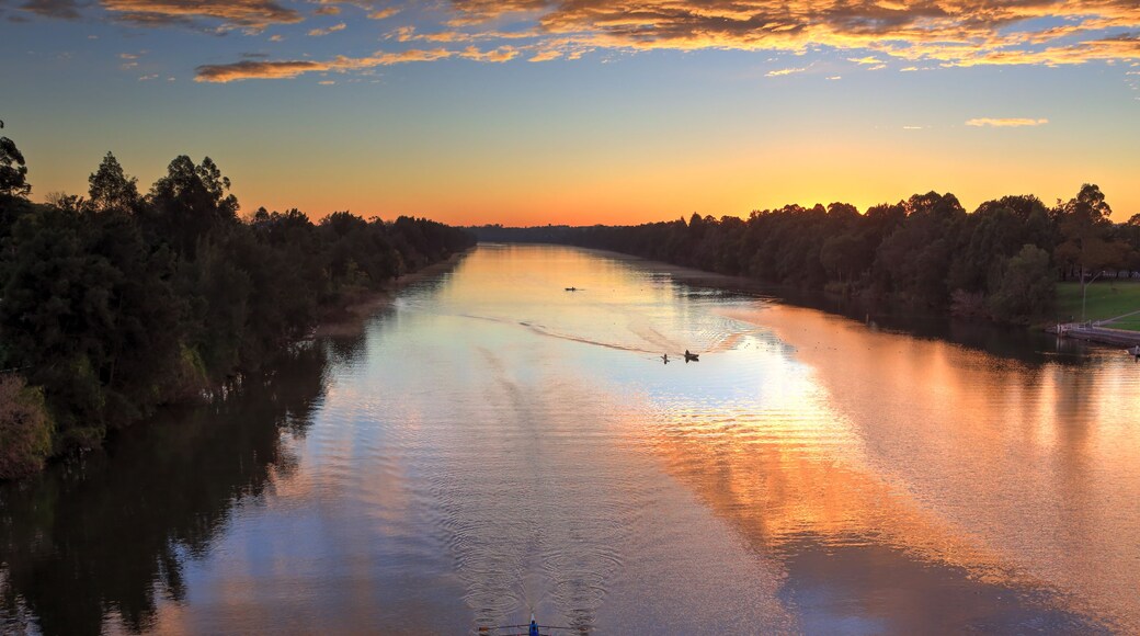 A river at sunset with a rowboat in the foreground and a bridge in the background.