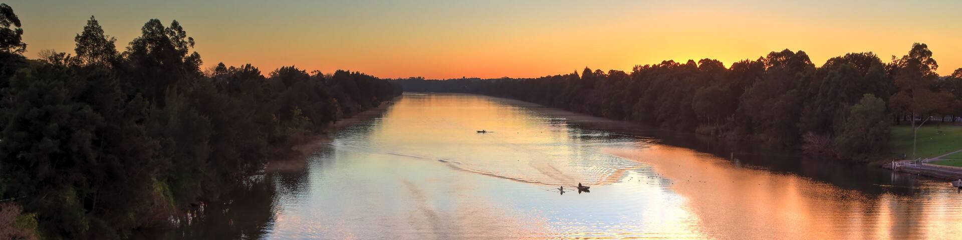 A river at sunset with a rowboat in the foreground and a bridge in the background.