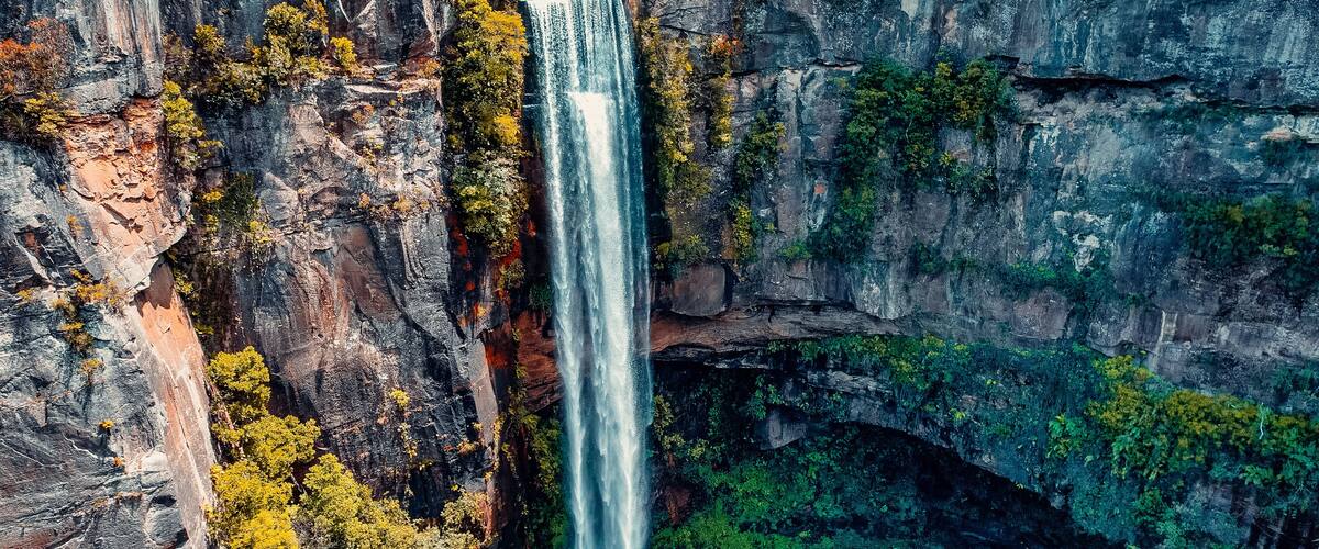 Uma cascata despencando por um penhasco rochoso, cercada por vegetação densa.