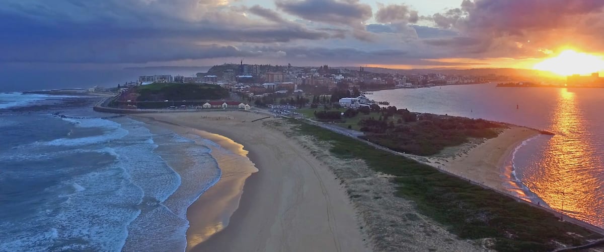 A coastal cityscape with a beach, ocean waves, and a sunset.