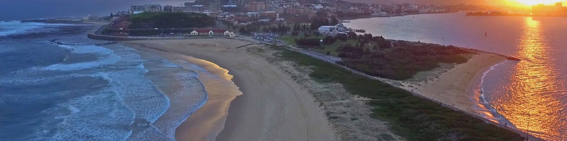 A coastal cityscape with a beach, ocean waves, and a sunset.