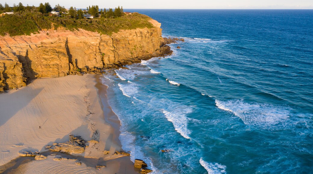 A coastal landscape with a sandy beach, rocky cliffs, and the ocean.