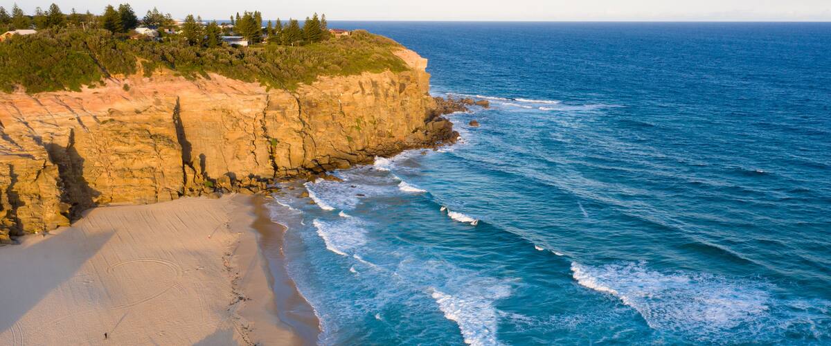 A coastal landscape with a sandy beach, rocky cliffs, and the ocean.