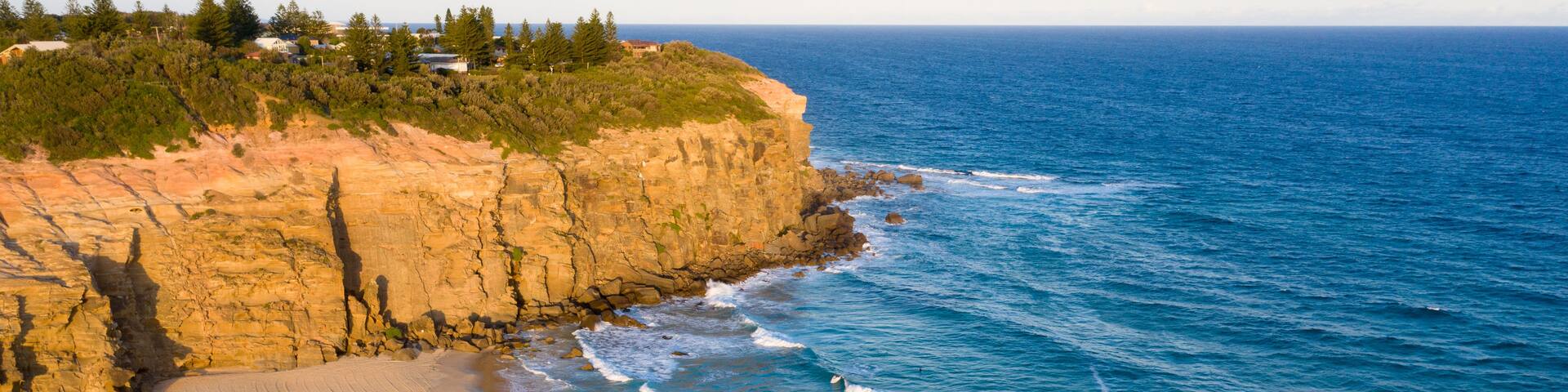 A coastal landscape with a sandy beach, rocky cliffs, and the ocean.