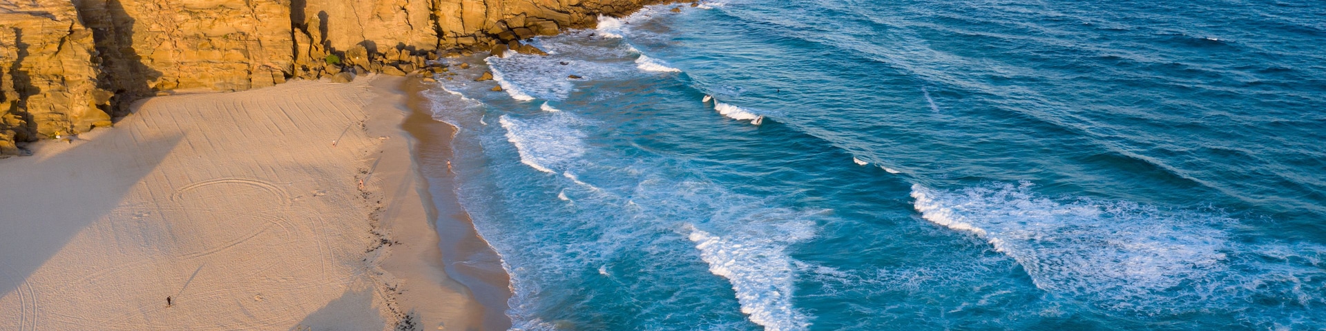 Paisagem costeira com praia arenosa, falésias rochosas e o oceano.