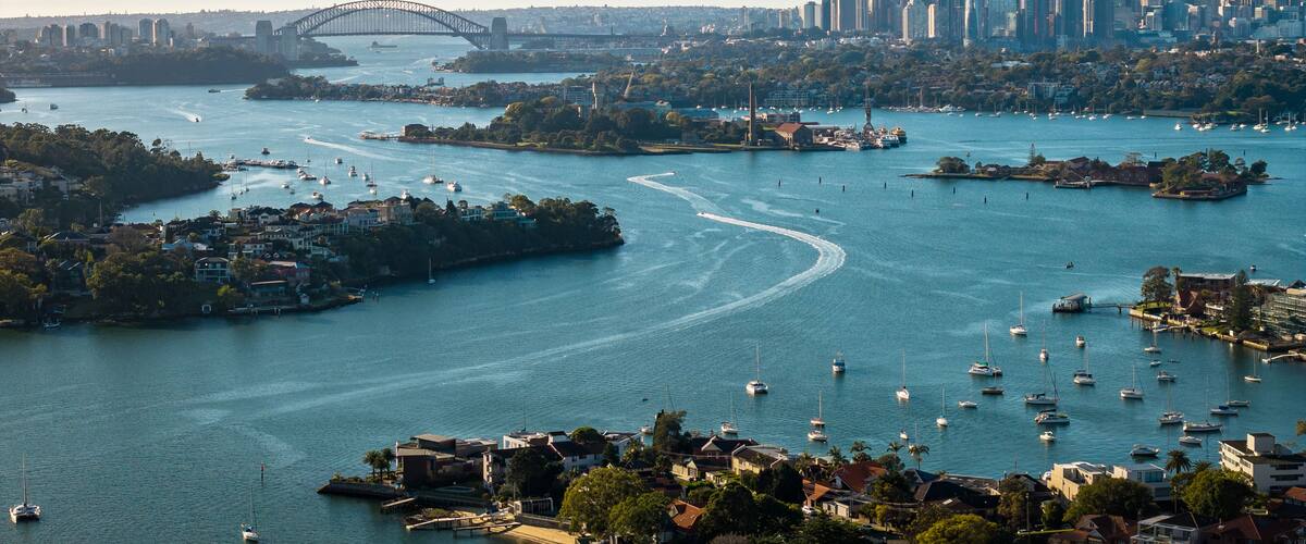 Un paisaje urbano costero con un puente destacado, numerosos barcos y un horizonte urbano denso.