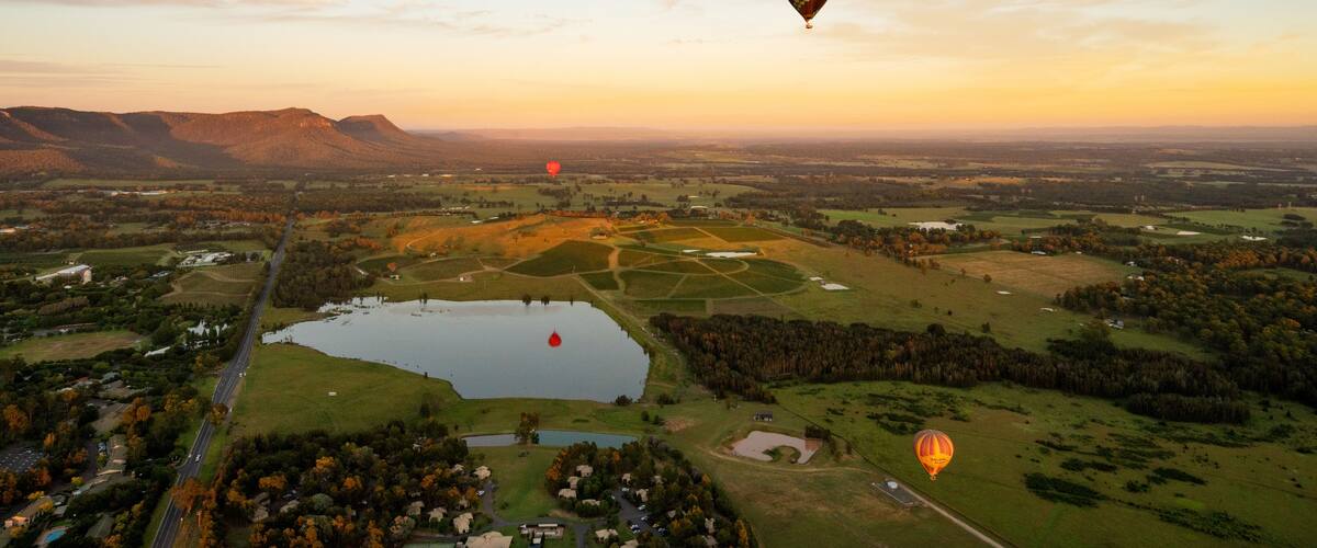 A landscape with multiple hot air balloons, a lake, and a road.