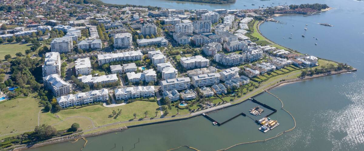An aerial view of a coastal residential area with modern apartment buildings, a marina, and a river.